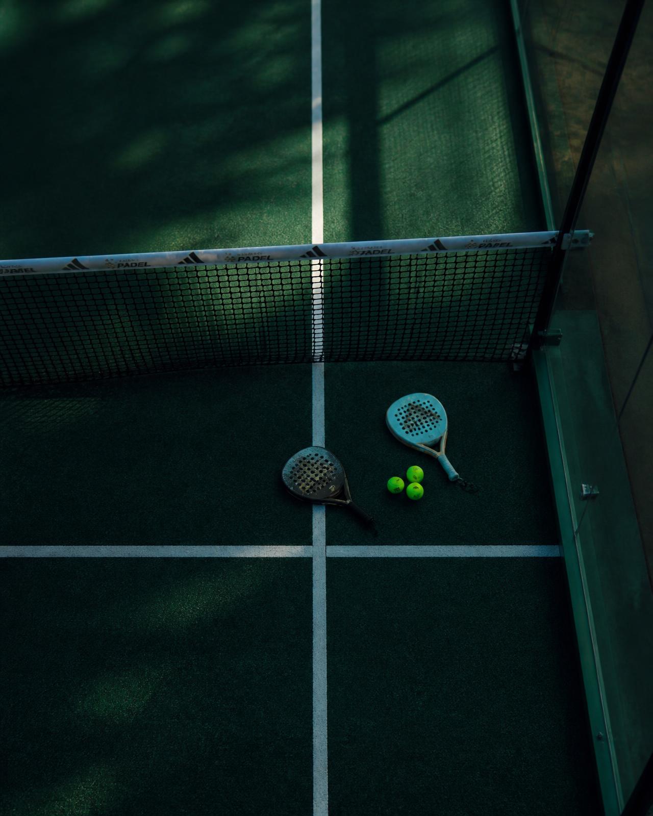 Padel court at dusk with rackets and balls beside the net